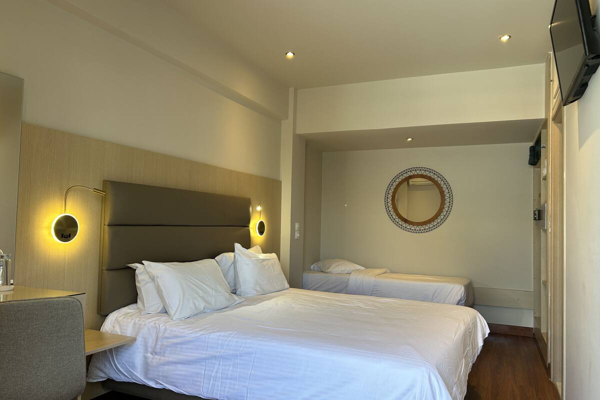 A hotel room with a large bed, a bedside table, a desk, and a round mirror on the wall.