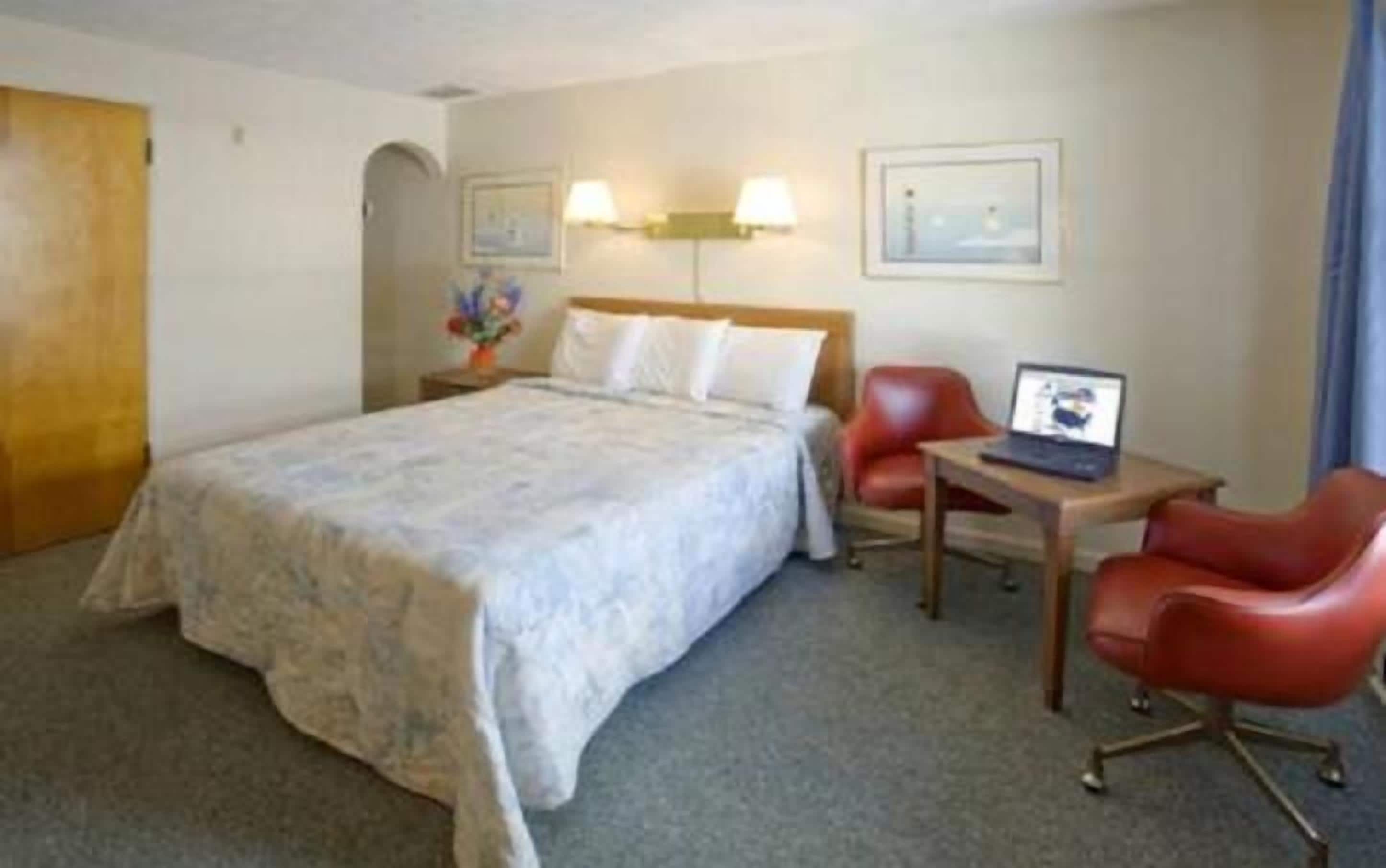Habitación de hotel con una cama, dos sillas, un escritorio con una computadora portátil y una lámpara.