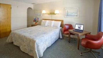 Habitación de hotel con una cama, dos sillas, un escritorio con una computadora portátil y una lámpara.