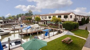 Un port de plaisance avec des bateaux amarrés, un bâtiment d’hôtel et une zone herbeuse équipée d’une table de pique-nique et d’un parasol.