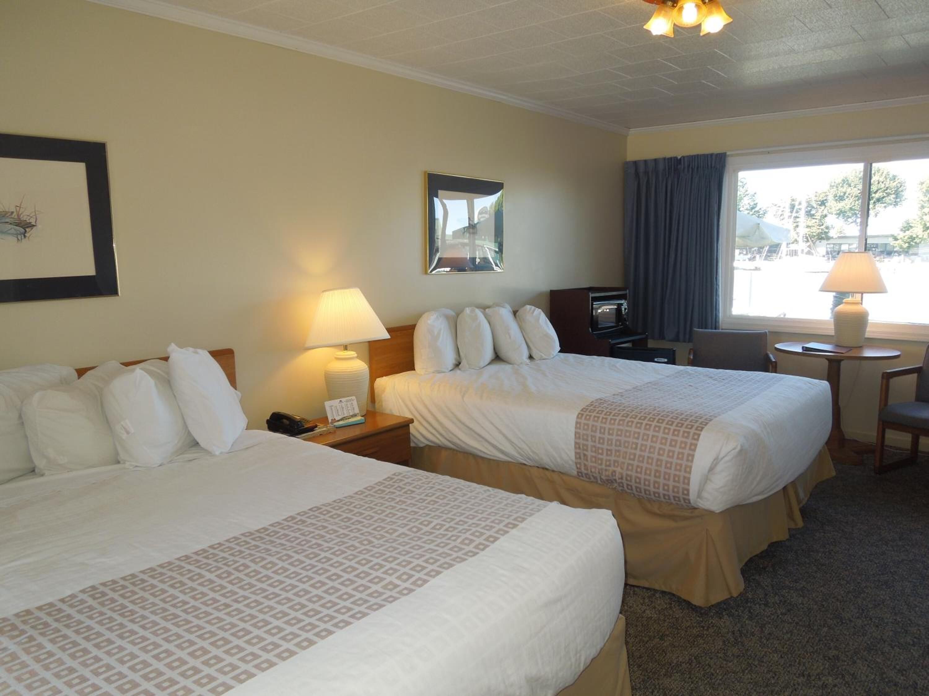 A hotel room with two beds, a desk, a chair, a lamp, a mirror, and a window with curtains.