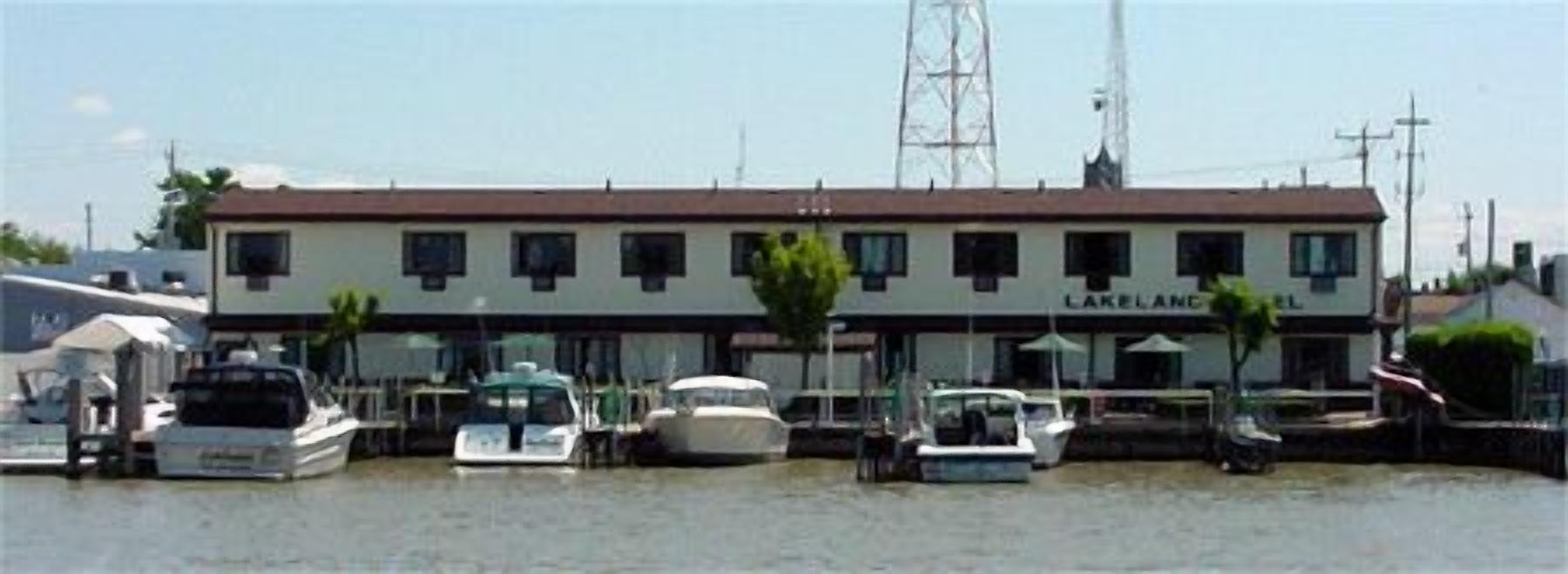 Ein Gebäude am Wasser, genannt „LAKELAND“, mit mehreren Booten, die vor Anker liegen.
