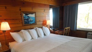 Une chambre de style cabane en bois, dotée d’un grand lit, de deux lampes de chevet, d’un bureau et d’une chaise.