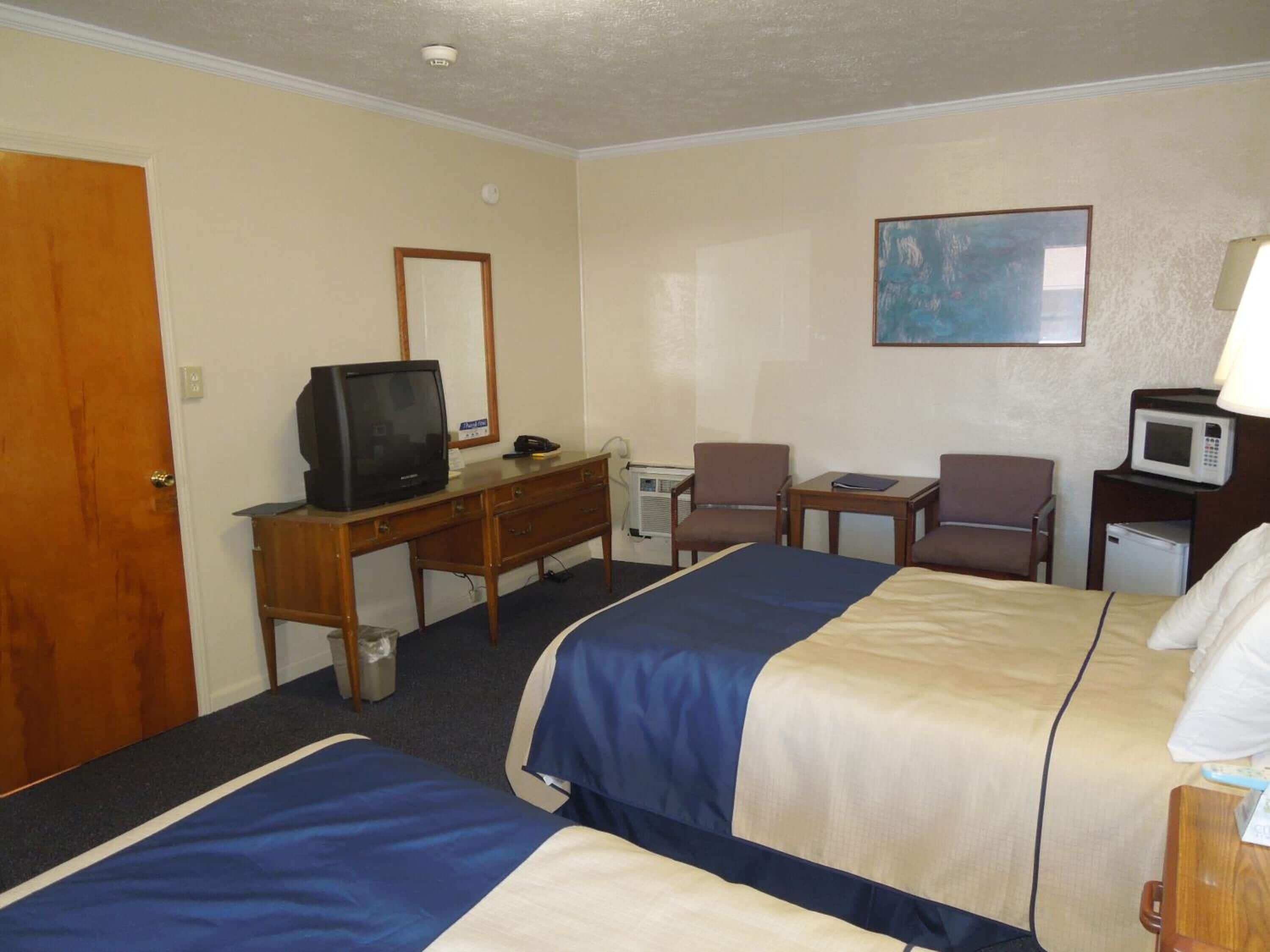 A hotel room with two beds, a desk with a television, a microwave, and a painting on the wall.