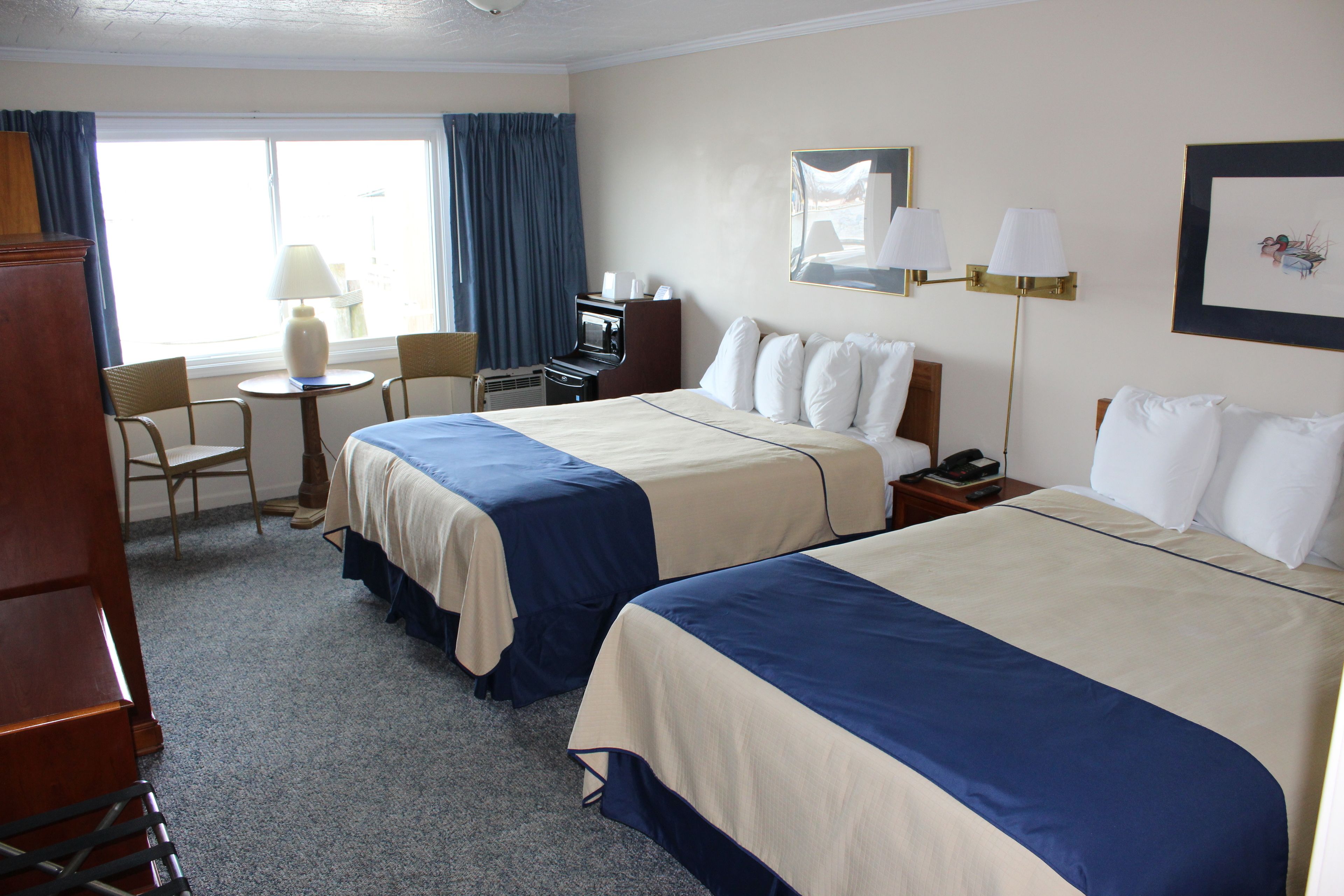 A hotel room with two beds, a desk, a chair, a lamp, and a window with curtains.