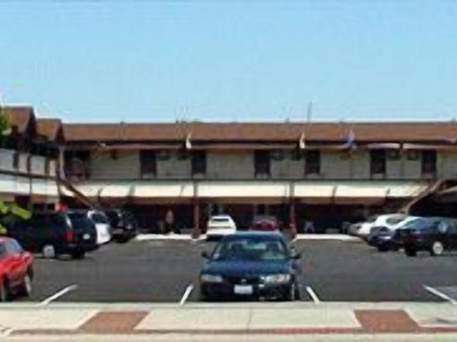 Un motel doté d’un parking central, où plusieurs voitures sont garées, et d’une rangée de bâtiments à toit plat.