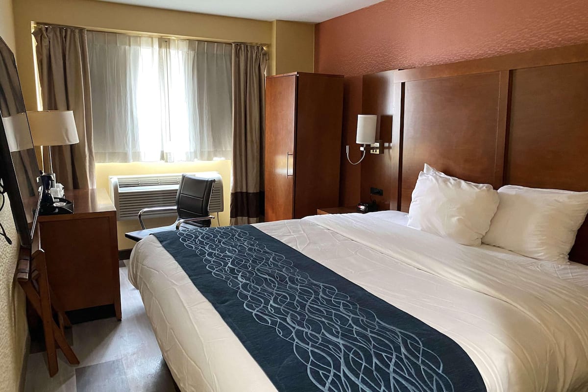 Une chambre d’hôtel avec un grand lit, un bureau avec une lampe, une armoire et une fenêtre avec des rideaux.