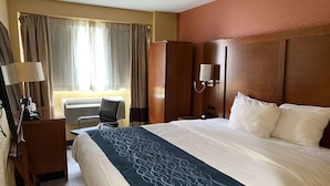 A hotel room with a large bed, a desk with a lamp, a chair, a wardrobe, and a window with curtains. - Ramada by Wyndham New York Times Square West (New York)
