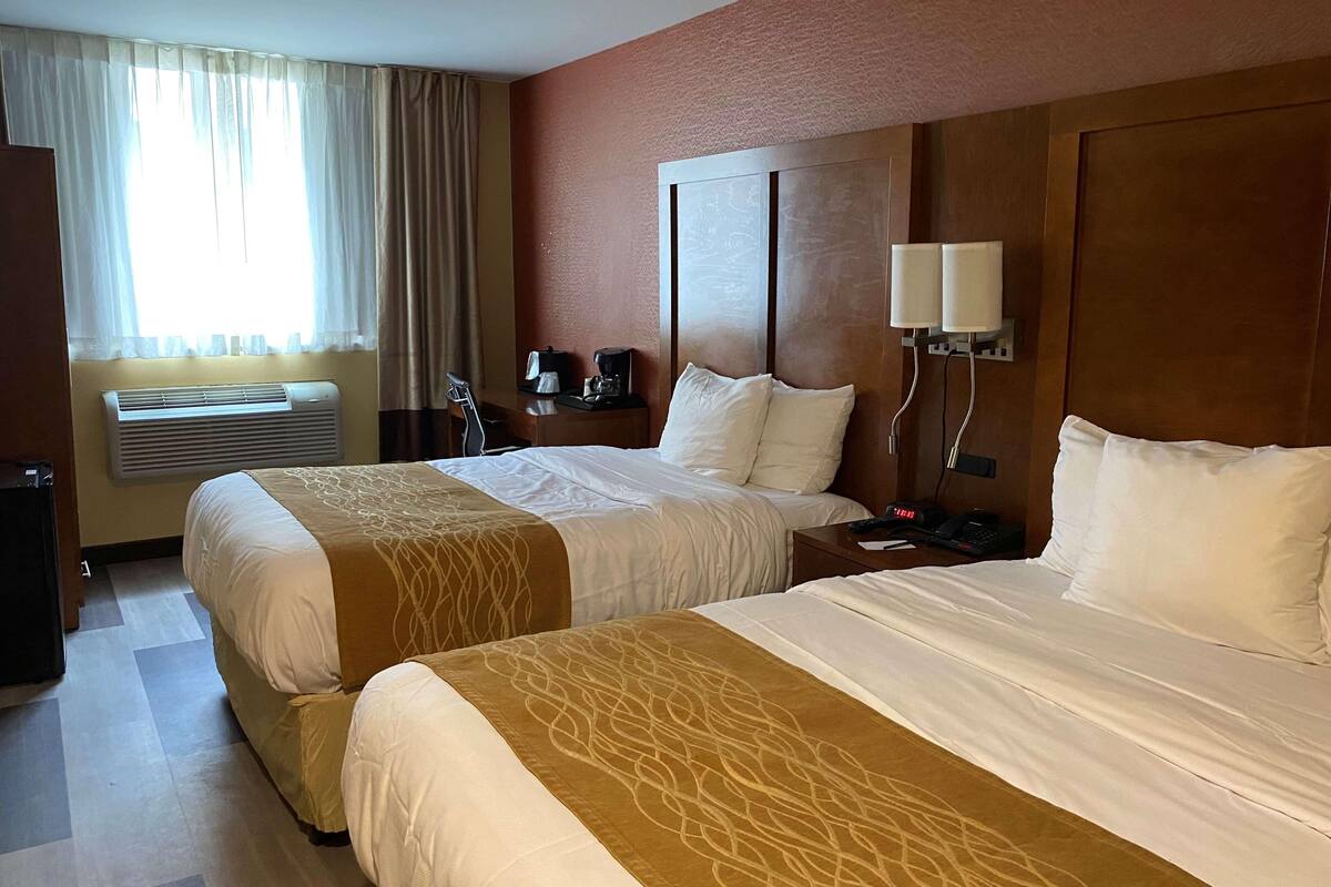 Une chambre d’hôtel avec deux lits, un bureau avec une machine à café, un téléphone et un appareil de climatisation.