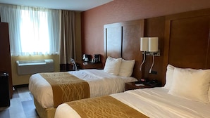 A hotel room with two beds, a desk with a coffee maker, a lamp, and an air conditioning unit. - Ramada by Wyndham New York Times Square West (New York)