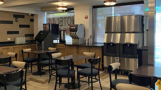 A modern kitchen area with stainless steel appliances, a coffee machine, and a seating area with tables and chairs. - Ramada by Wyndham New York Times Square West (New York)