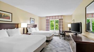 A hotel room with two beds, a desk, a television, and a window with a view of greenery.