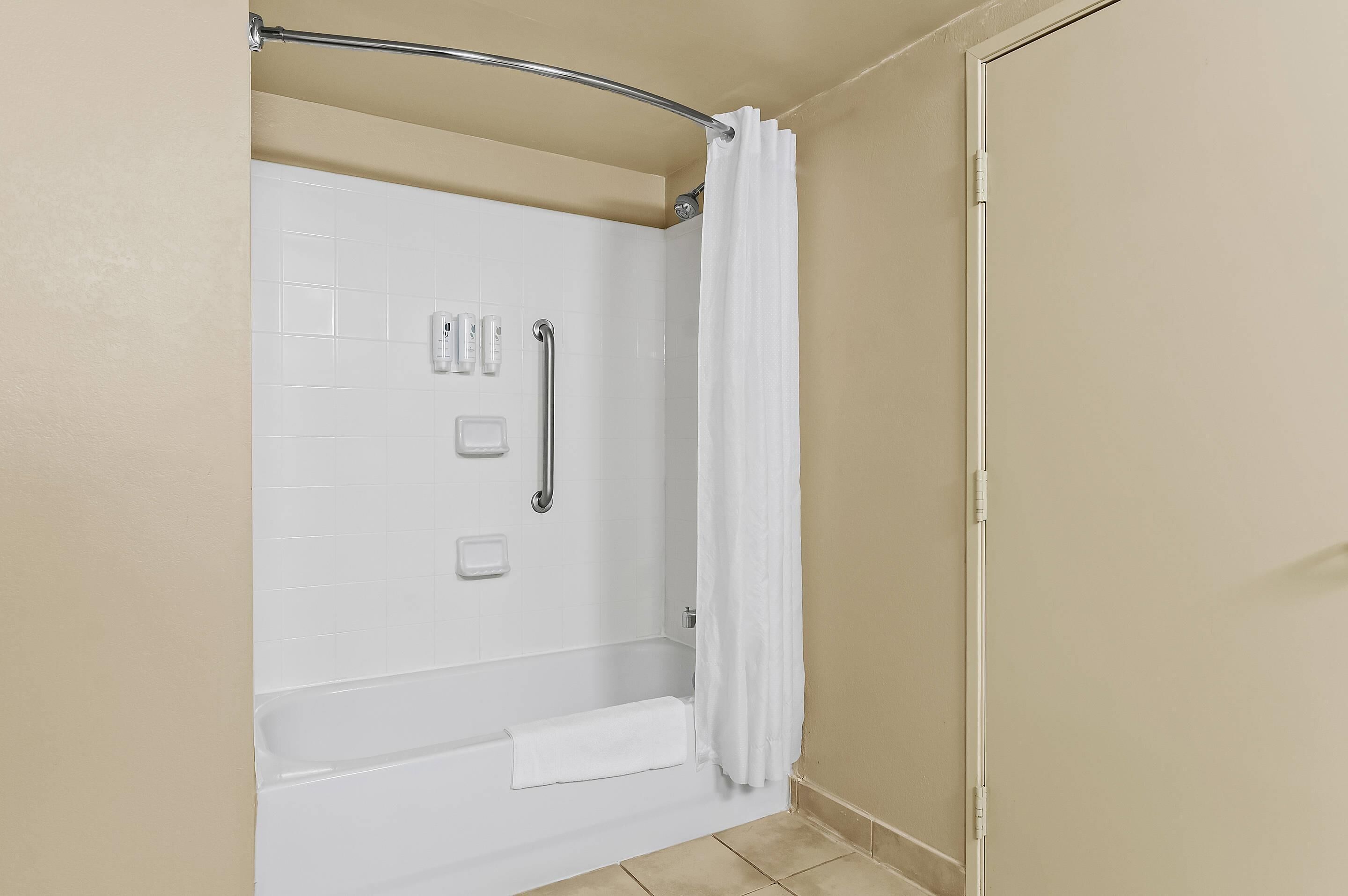 Un espace douche avec un mur recouvert de carreaux blancs, une barre d’appui, un porte-serviettes et un rideau de douche.