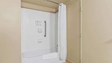 Un espace douche avec un mur recouvert de carreaux blancs, une barre d’appui, un porte-serviettes et un rideau de douche.