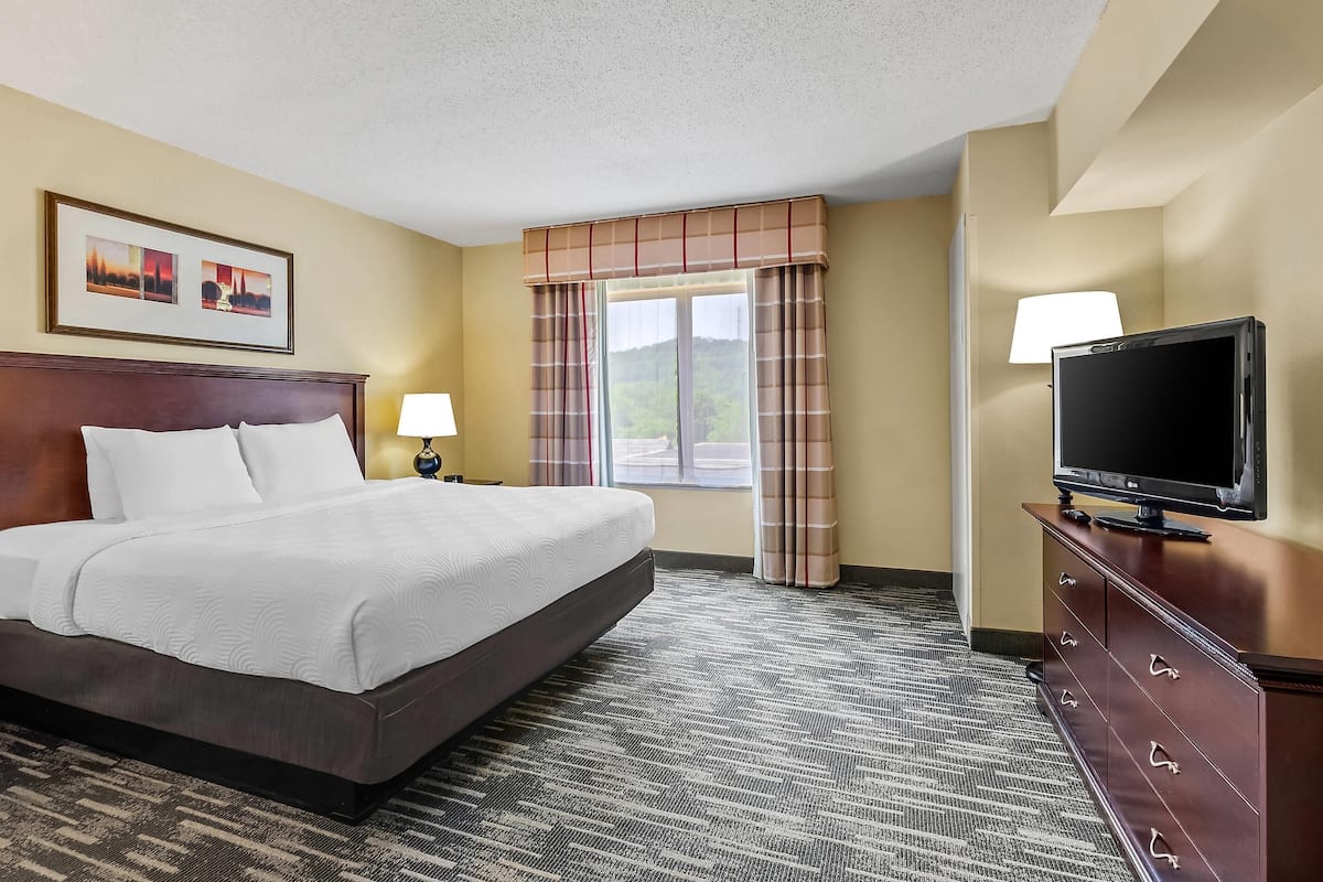 A hotel room with a large bed, a television on a dresser, and a window with curtains.