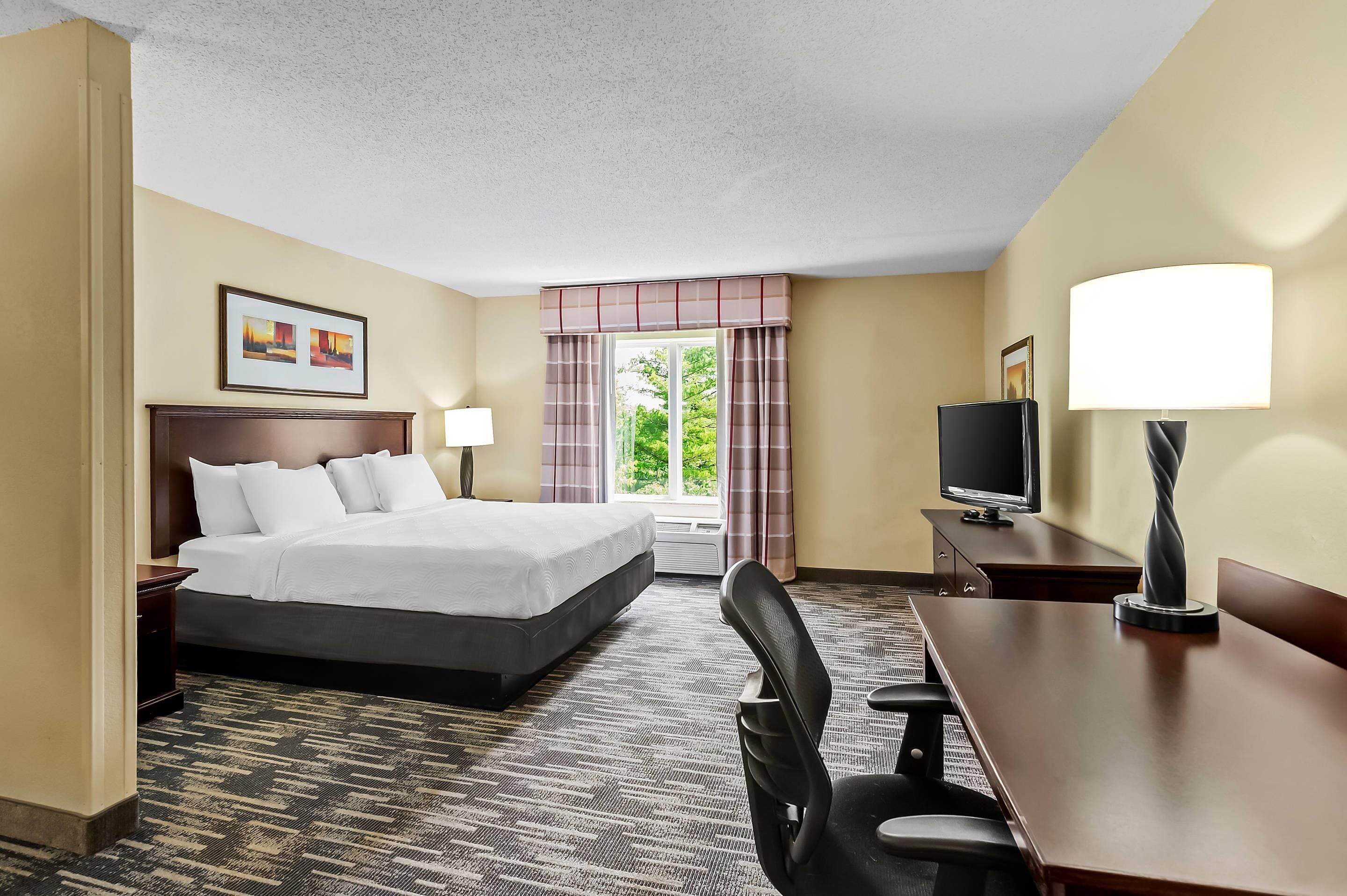 A hotel room with a bed, desk, chair, TV, and a window with curtains.