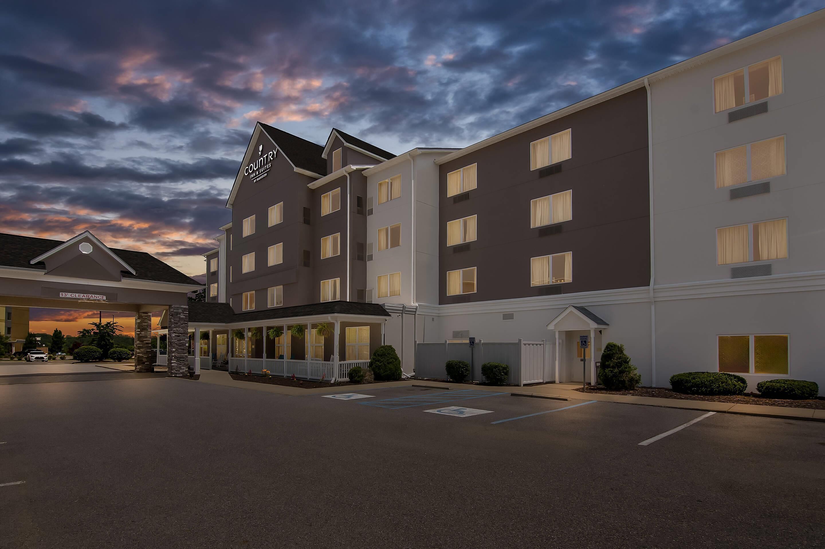 A hotel with a modern design, featuring a prominent 'Country Inn & Suites' sign, a well-lit entrance, and a spacious parking area.