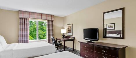 Une chambre d’hôtel comprenant un lit, un bureau avec une chaise, une télévision, une commode et une fenêtre avec des rideaux.