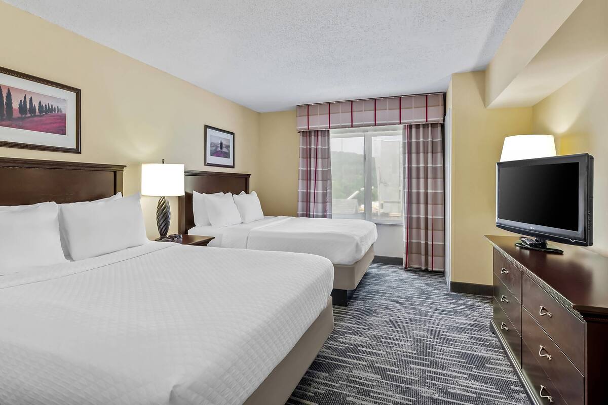 A hotel room with two beds, a television, a dresser, and a window with curtains.