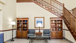 Un salón espacioso con una mesa de centro de vidrio, dos sofás y armarios de madera. Se ve una escalera al fondo.