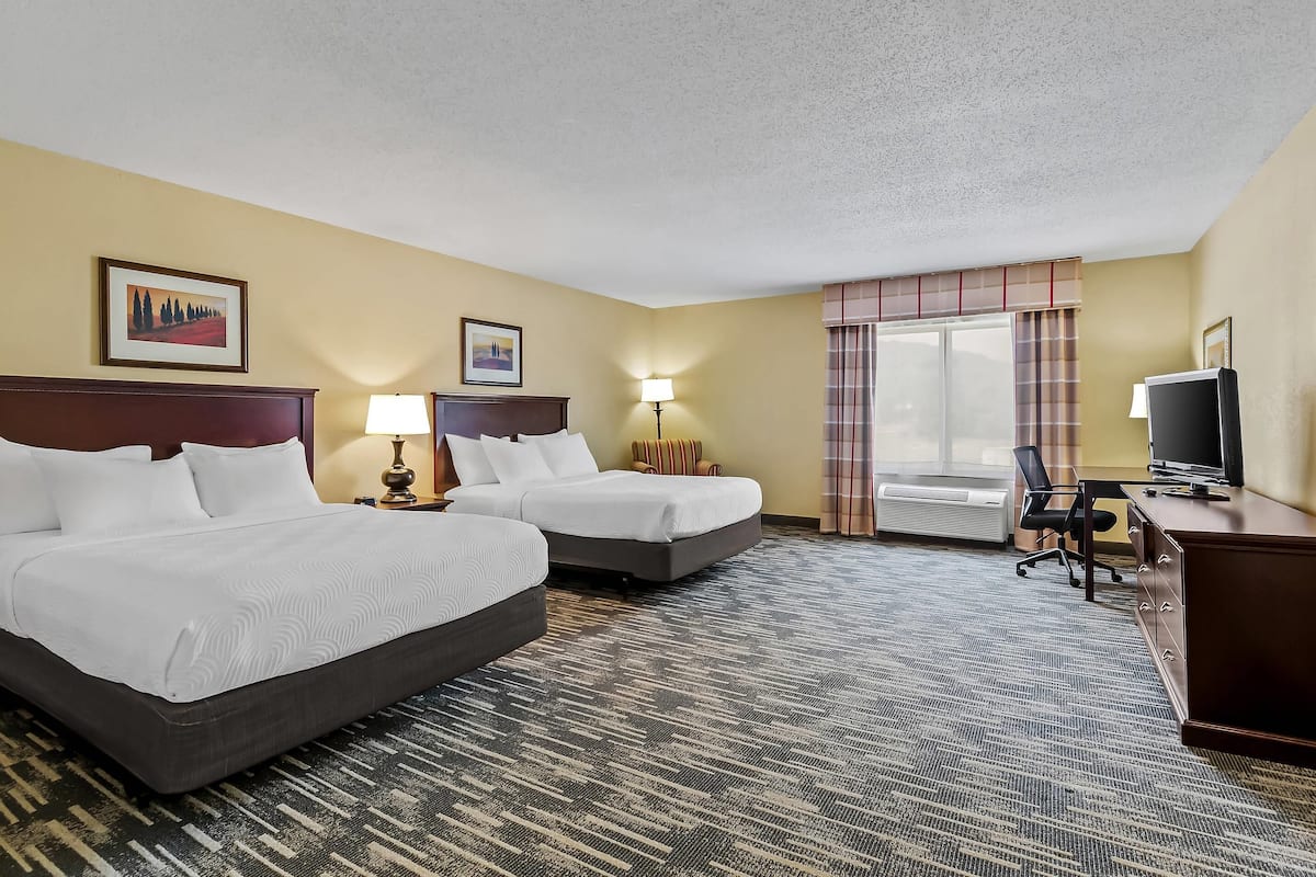 A hotel room with two beds, a desk, a TV, and a window with curtains.