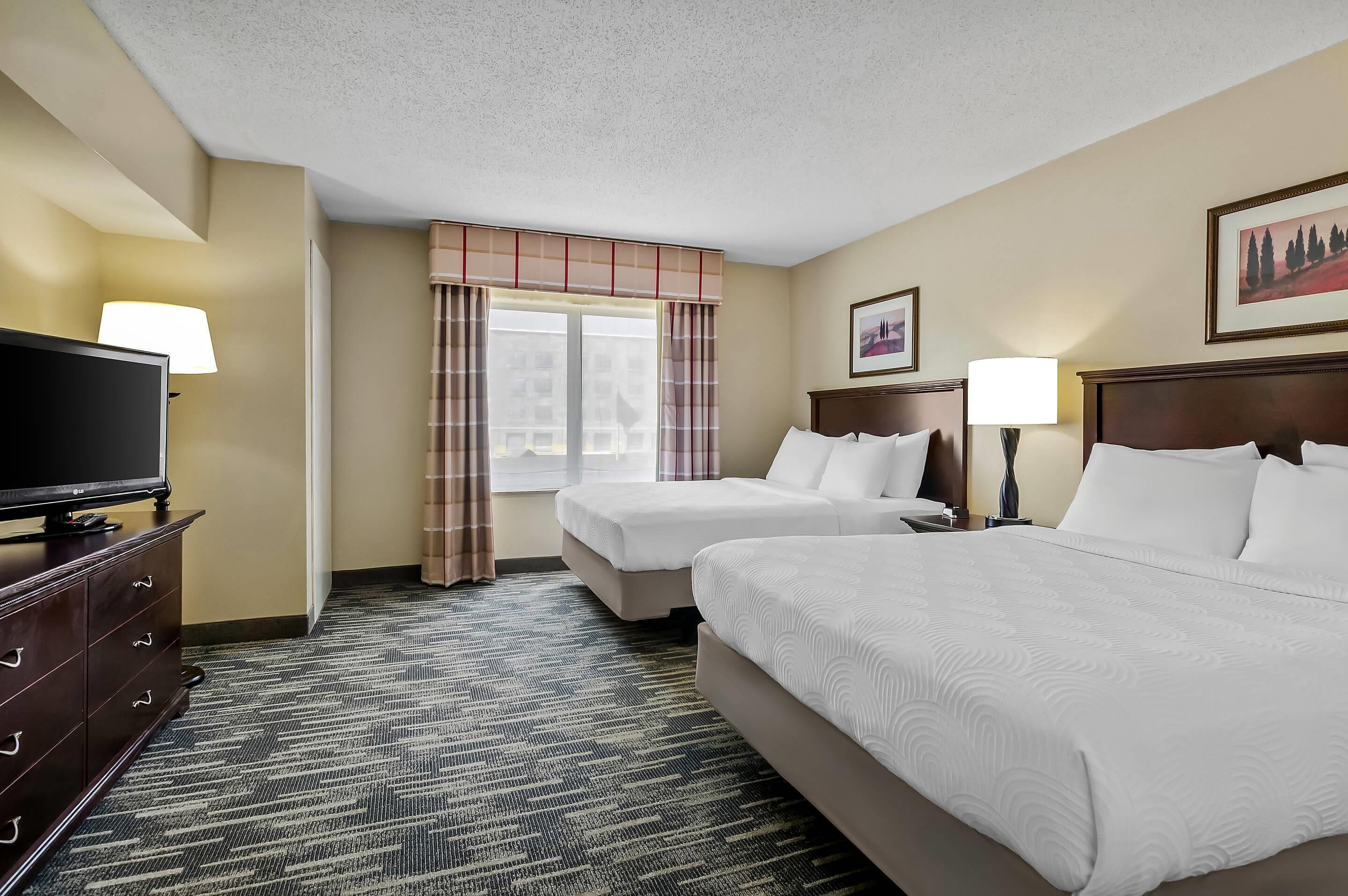 A hotel room with two beds, a TV, a dresser, and a window with curtains.
