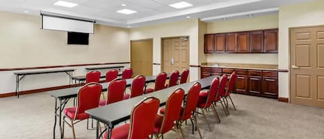 A conference room with a long table and red chairs, a projector screen, and a kitchenette area.