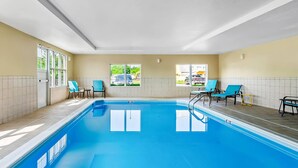 An indoor swimming pool with clear blue water, tiled walls, and several blue lounge chairs.