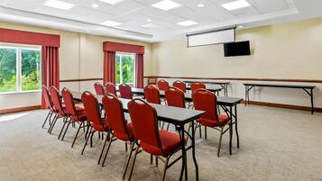 A conference room with a large table and chairs, a projector screen, and a view of greenery outside.