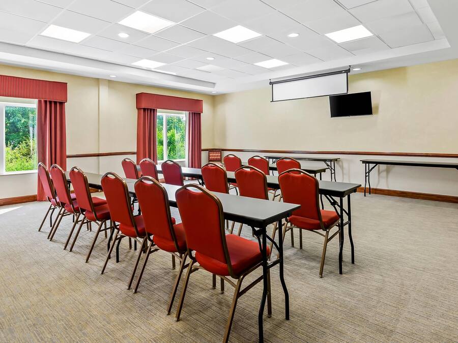 A conference room with a large table and chairs, a projector screen, and a view of greenery outside.
