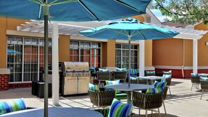 Une terrasse extérieure avec des tables et des chaises rondes, un barbecue et des parasols pour faire de l’ombre.