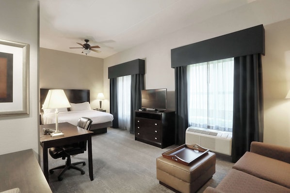 A hotel room with a bed, desk, chair, television, and a sofa.