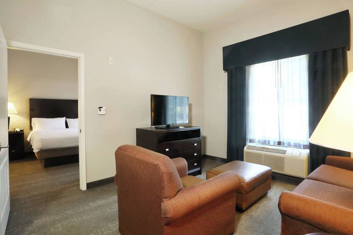Habitación de hotel con cama, televisor en una cómoda, escritorio y ventana con cortinas.