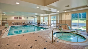Une piscine intérieure dotée de chaises longues et d’un jacuzzi, le tout entouré de grandes fenêtres.