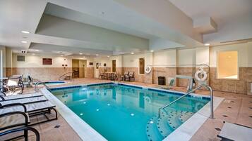 Una piscina interior con agua cristalina, rodeada de sillones de descanso y mesas, y un suelo de baldosas.