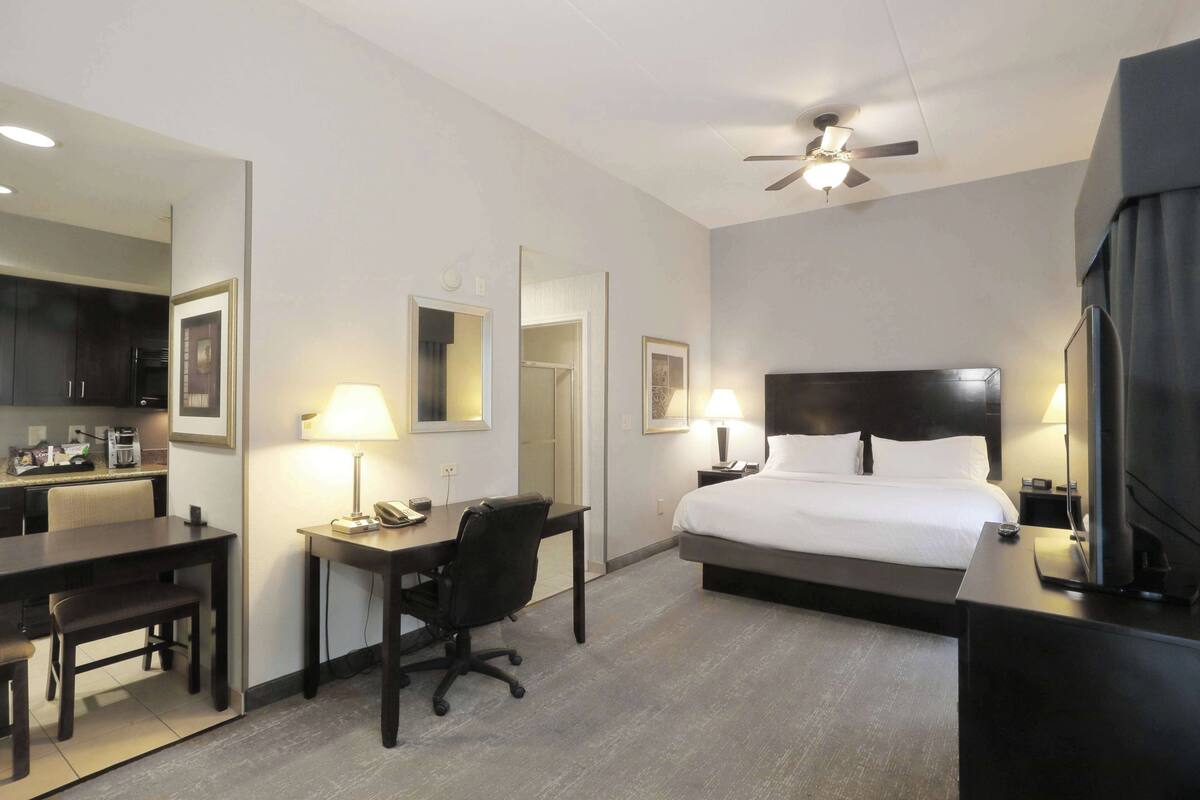 Una habitación de hotel con cama, escritorio, silla y ventilador de techo.