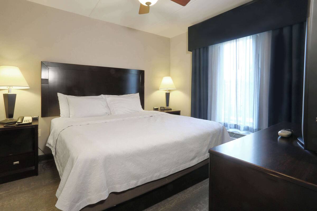 Habitación de hotel con una cama grande, dos mesitas de noche con lámparas, un escritorio y una ventana con cortinas.