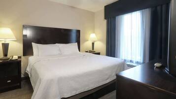 A hotel room with a large bed, two bedside tables with lamps, a desk, and a window with curtains.