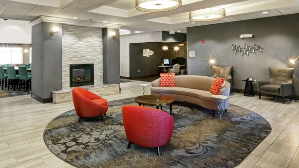 Un hall d’entrée moderne avec un canapé incurvé, des fauteuils rouges, une cheminée et un coin repas avec des chaises vertes.