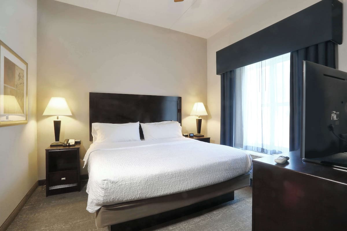 Una habitación de hotel con una cama grande, dos mesitas de noche con lámparas, un televisor de pantalla plana y una ventana con cortinas.