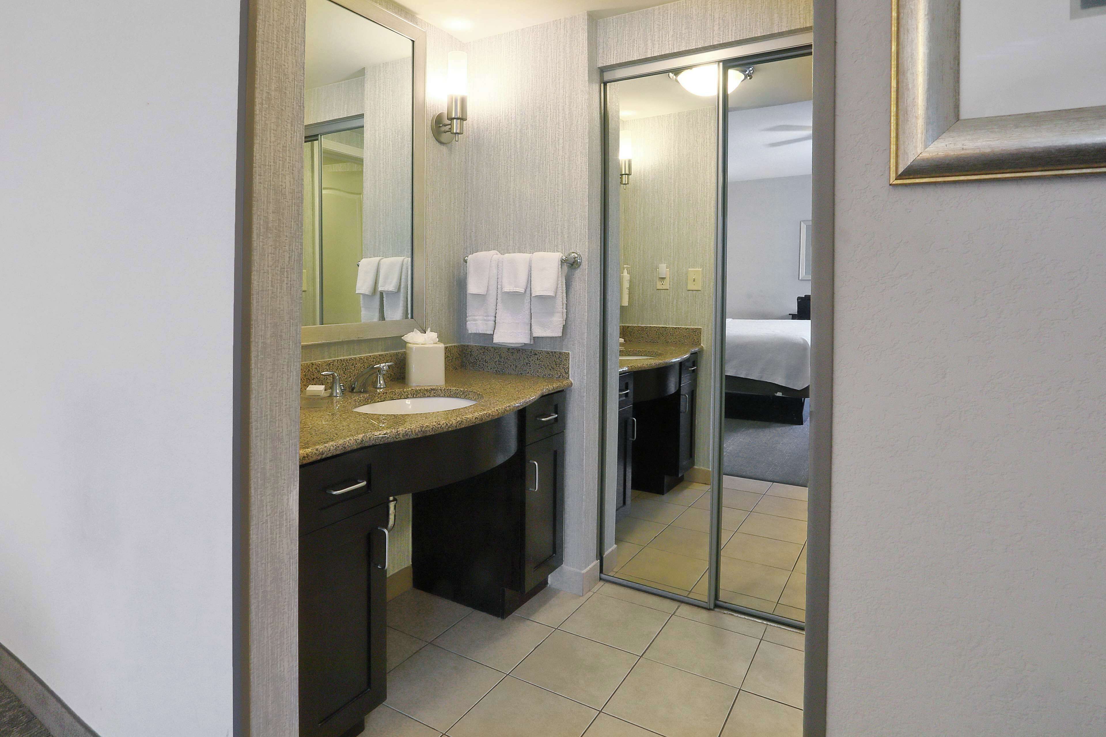 A hotel bathroom with a sink, mirror, and towel rack.