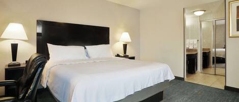 Habitación de hotel con una cama grande, dos lámparas de noche, una silla y un baño visible a través de una puerta abierta.