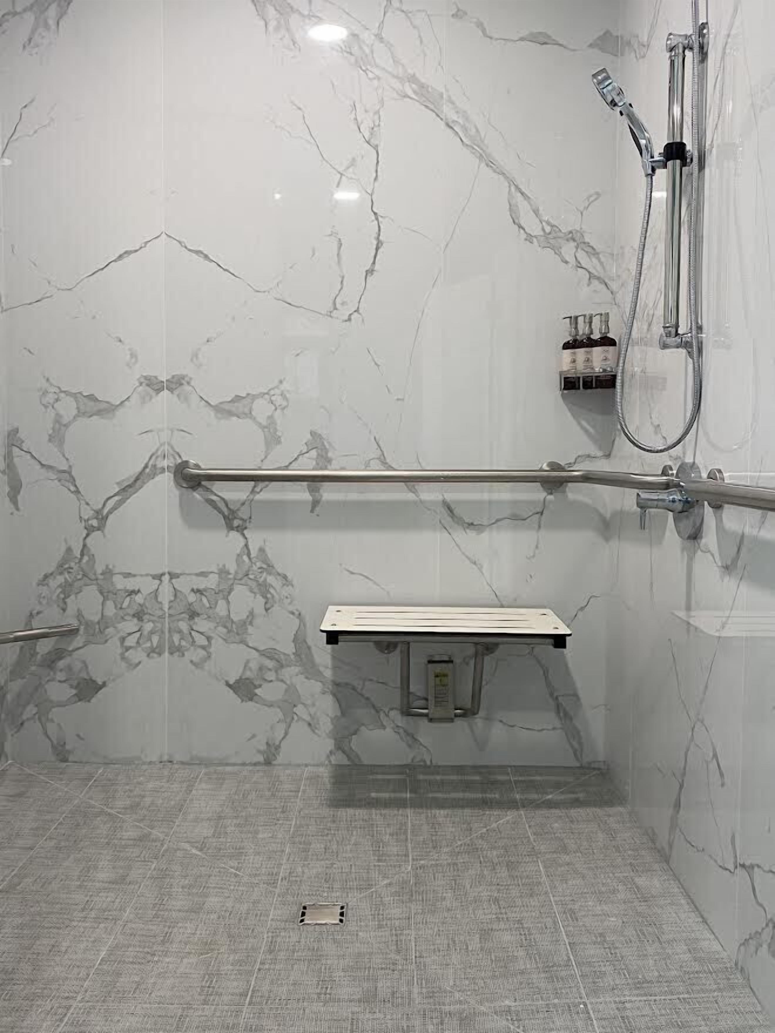 A modern bathroom with marble walls, a glass shower enclosure, and a grab bar.