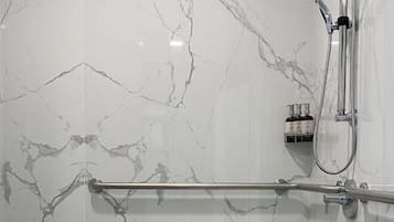 A modern bathroom with marble walls, a glass shower enclosure, and a grab bar.