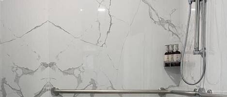 A modern bathroom with marble walls, a glass shower enclosure, and a grab bar.