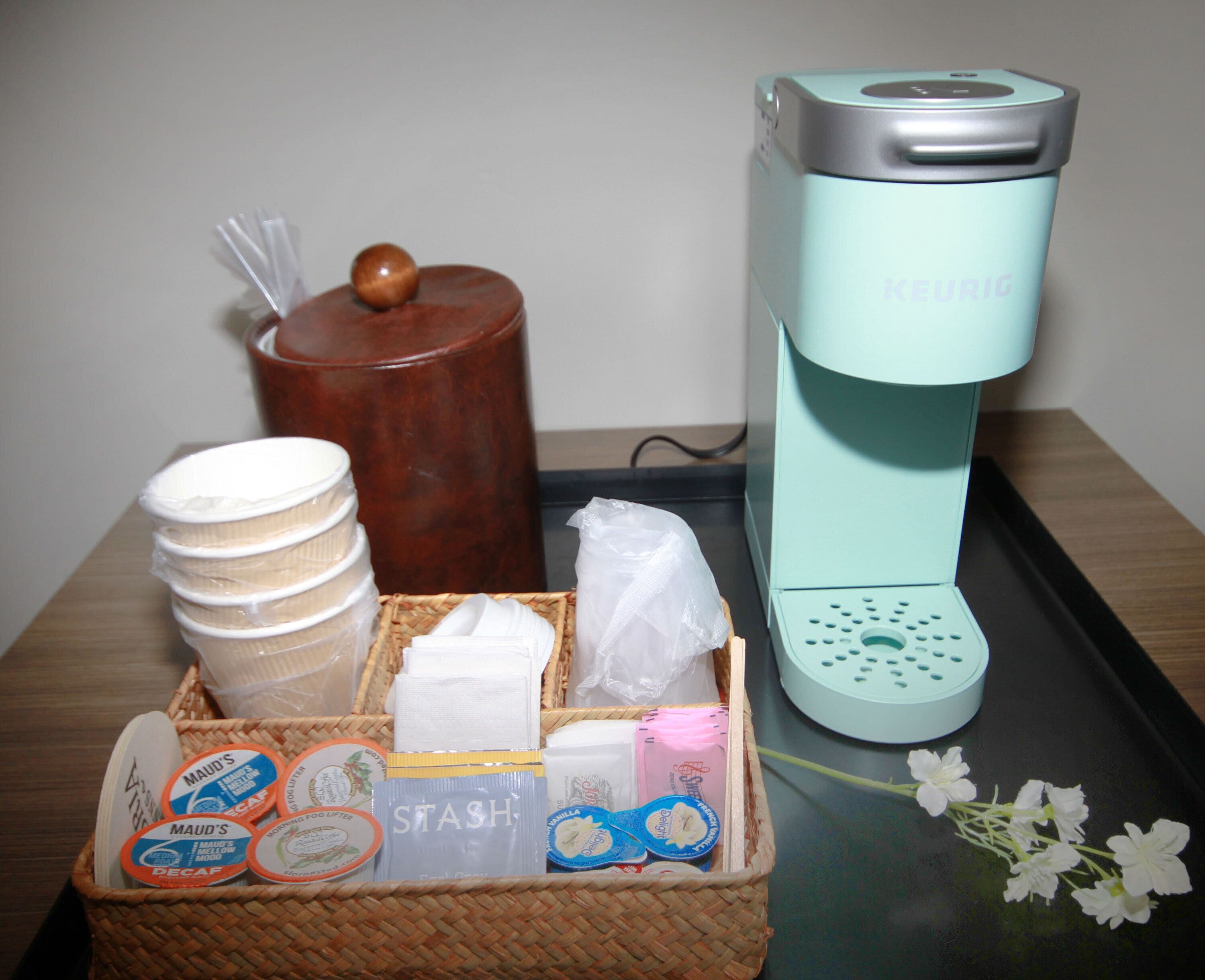 A coffee maker, a basket of toiletries, and a container with a lid on a table.