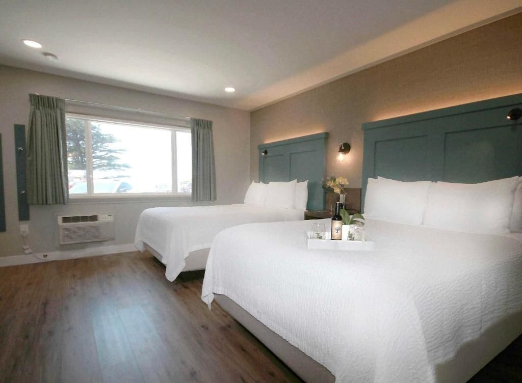 A hotel room with two beds, a large window, and a tray with items on the bed.