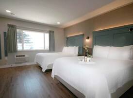 Habitación de hotel con dos camas, un ventanal grande y una bandeja con objetos sobre la cama.