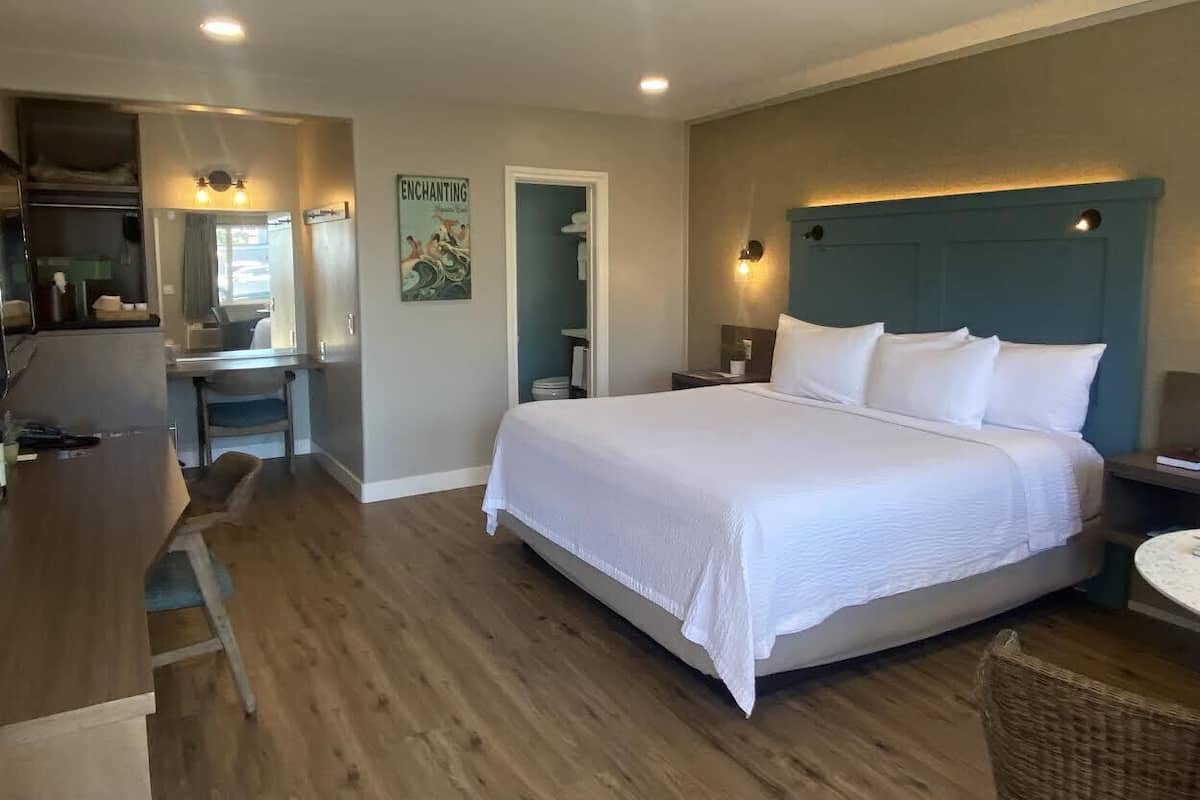 A hotel room with a bed, a desk, and a chair. There is a bathroom visible through an open door.