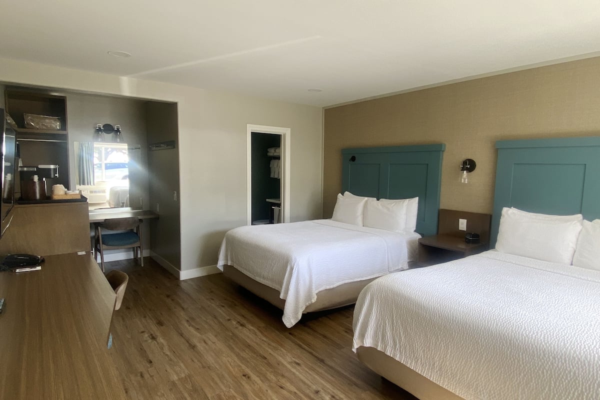 A hotel room with two beds, a desk, and a bathroom.